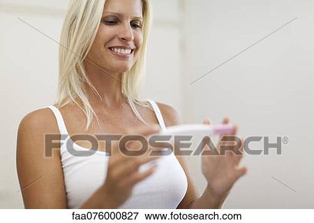 Stock Photo - Mid-adult woman looking at pregnancy test with cheerful expression. Fotosearch