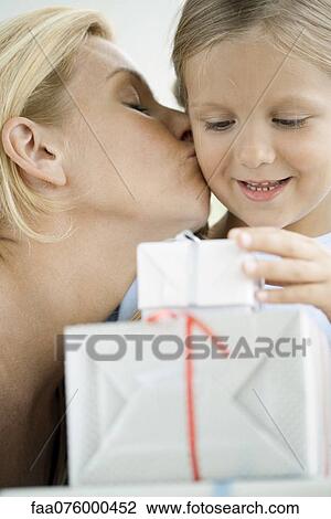 Mother kissing young daughter's cheek as girl looks at wrapped gifts View Large Photo Image Stock Image - Mother kissing young daughter's cheek as girl looks at wrapped gifts. Fotosearch