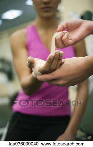 Stock Image - Person wrapping bandage around woman's hand, cropped. Fotosearch