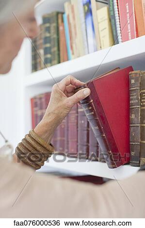 Stock Photograph - Senior woman choosing book from bookshelf. Fotosearch