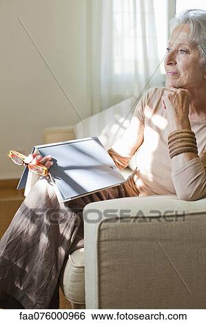Stock Photograph - Senior woman relaxing on sofa with book. Fotosearch