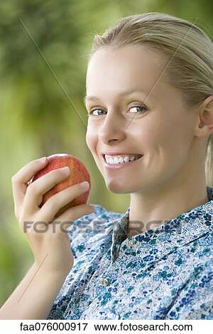 Stock Photo - Smiling young woman holding apple, portrait. Fotosearch