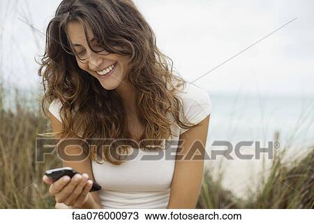 Stock Image - Smiling young woman looking at cell phone. Fotosearch