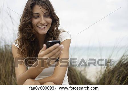 Smiling young woman looking at cell phone View Large Photo Image Stock Photo - Smiling young woman looking at cell phone. Fotosearch