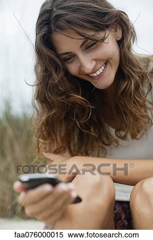 Smiling young woman looking at cell phone View Large Photo Image Stock Photography - Smiling young woman looking at cell phone. Fotosearch