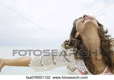 Stock Image - Smiling young woman with arms out, low angle view. Fotosearch