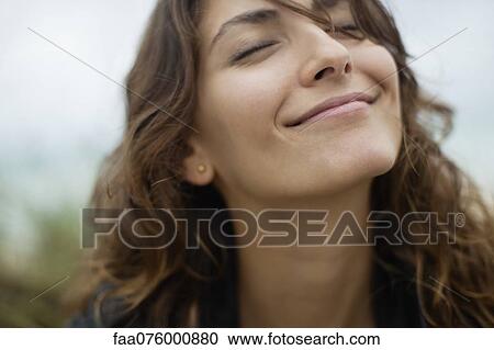 Stock Image - Smiling young woman with eyes closed. Fotosearch