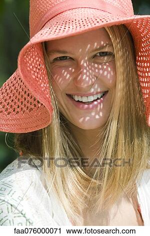 Stock Image - Smiling young woman with straw hat, portrait. Fotosearch
