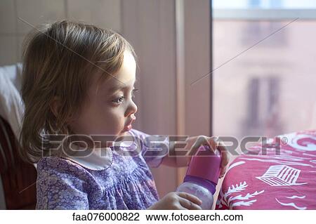 Stock Image - Toddler girl holding baby bottle, looking away in thought. Fotosearch