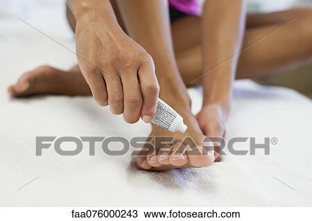 Stock Image - Woman applying ointment to foot, low section. Fotosearch