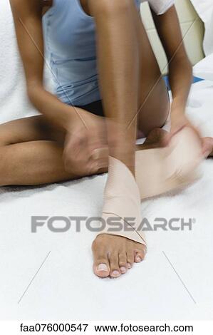 Stock Photo - Woman bandaging foot and ankle, cropped. Fotosearch