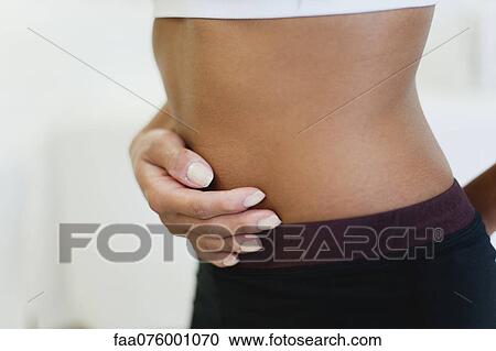 Stock Image - Woman holding stomach, mid section. Fotosearch