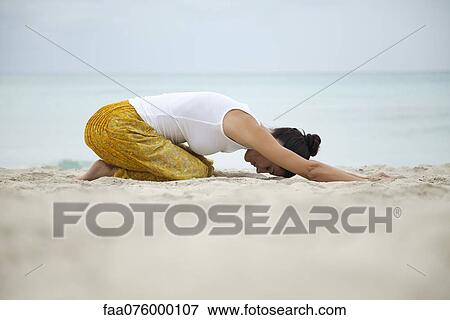 Stock Photo - Woman in childs pose on beach, side view. Fotosearch