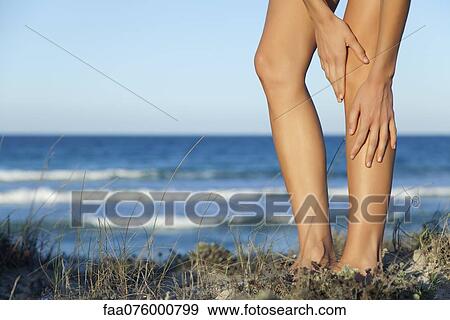 Stock Photo - Woman rubbing legs on beach, low section. Fotosearch