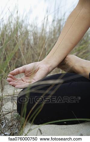 Stock Image - Woman sitting in lotus position, fingers in meditation position, cropped. Fotosearch