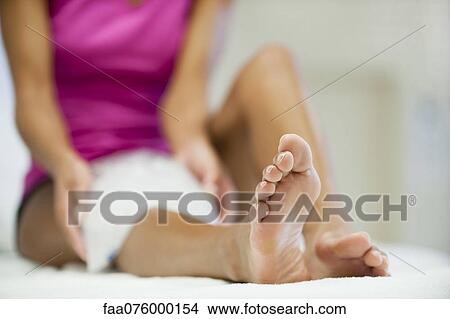 Picture - Woman sitting with ice pack on knee, focus on foreground. Fotosearch