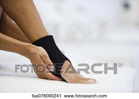 Stock Image - Woman wearing ankle brace, low section. Fotosearch
