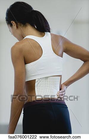 Stock Image - Woman with bandage on lower back, rear view. Fotosearch