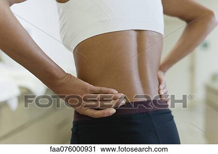 Stock Image - Woman with hands on lower back, mid section. Fotosearch