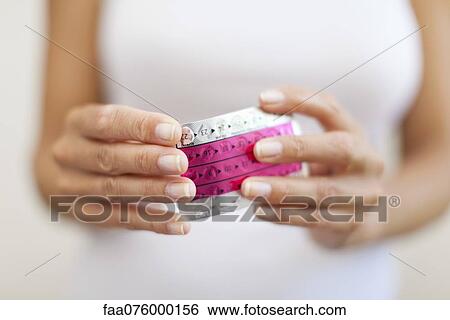 Stock Photograph - Woman's hand holding birth control pills, cropped. Fotosearch