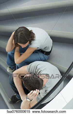 Stock Photography - Young couple sitting on stairs, hugging knees and talking. Fotosearch
