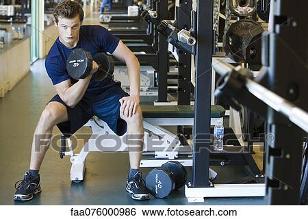 Young man lifting dumbbell in weight room View Large Photo Image Stock Photograph - Young man lifting dumbbell in weight room. Fotosearch