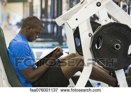 Young man reading book while lifting weights View Large Photo Image Stock Photo - Young man reading book while lifting weights. Fotosearch