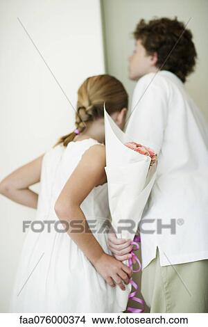 Picture - Young siblings holding bouqet of flowers behind backs, peeking through doorway. Fotosearch