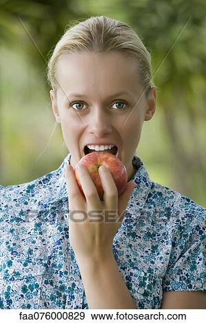 Stock Photo - Young woman biting into apple, portrait. Fotosearch
