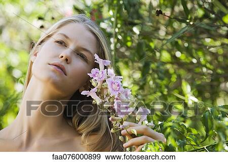Stock Photo - Young woman holding branch of flowers, looking up, portrait. Fotosearch