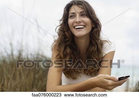 Stock Image - Young woman holding cell phone, selective focus. Fotosearch