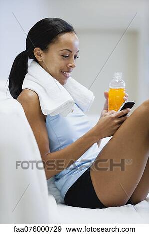 Stock Photo - Young woman relaxing with sports drink and text messaging with cell phone. Fotosearch
