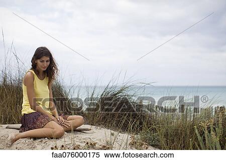 Stock Photography - Young woman sitting on beach. Fotosearch