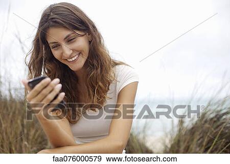 Young woman smiling at cell phone View Large Photo Image Stock Photo - Young woman smiling at cell phone. Fotosearch
