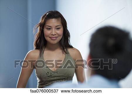 Stock Photo - Young woman smiling flirtatiously at man in foreground. Fotosearch