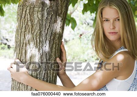 Stock Image - Young woman touching tree trunk, portrait. Fotosearch