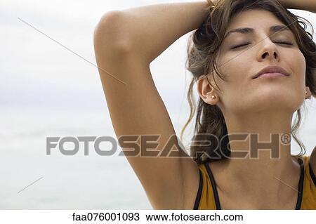 Stock Image - Young woman with hands on head and eyes closed, cropped. Fotosearch