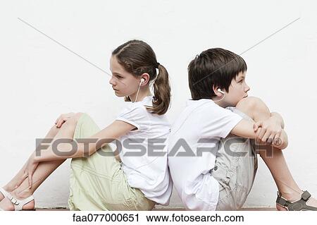 Stock Image - Boy and girl sitting back to back listening to music together. Fotosearch