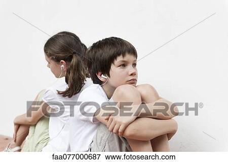 Stock Photo - Boy and girl sitting back to back listening to music with earphones. Fotosearch