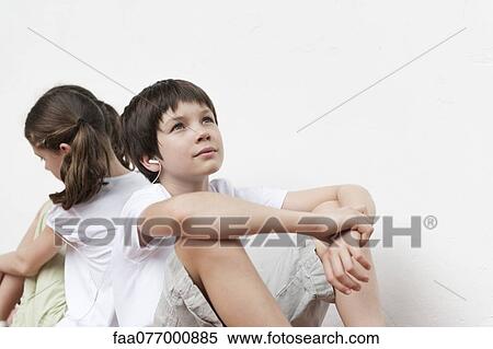 Stock Photography - Boy and girl sitting back to back listening to music with earphones. Fotosearch