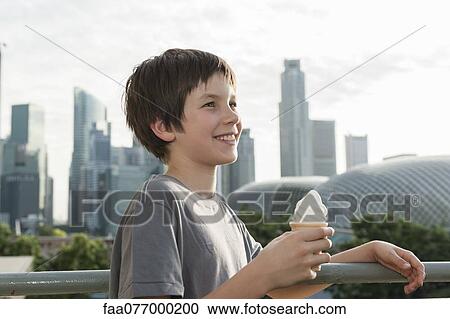 Stock Image - Boy holding ice cream cone, city skyline in background. Fotosearch
