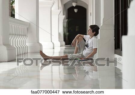 Stock Photo - Boy sitting on floor of veranda daydreaming. Fotosearch