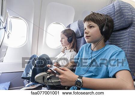 Stock Image - Boy using remote control to change channels on airplane. Fotosearch