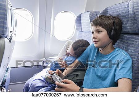 Stock Photo - Boy using remote control to change channels on airplane. Fotosearch