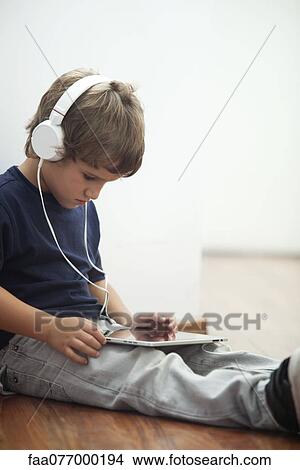 Picture - Boy wearing headphones and looking at digital tablet. Fotosearch