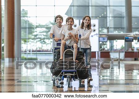 Brother and sister pushing younger sister on luggage cart in airport View Large Photo Image Stock Image - Brother and sister pushing younger sister on luggage cart in airport. Fotosearch