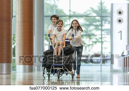Stock Photography - Brother and sister pushing younger sister on luggage cart in airport. Fotosearch
