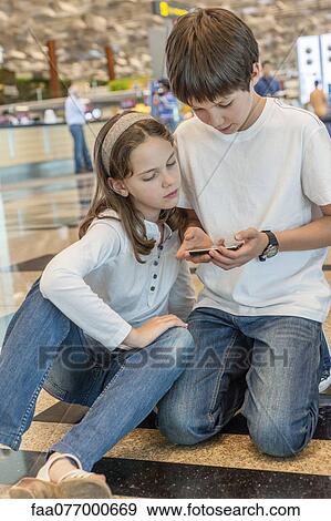 Stock Photo - Brother playing with cell phone, sister watching with interest. Fotosearch