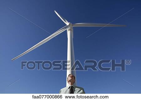 Stock Photograph - Businessman leaning against wind turbine. Fotosearch
