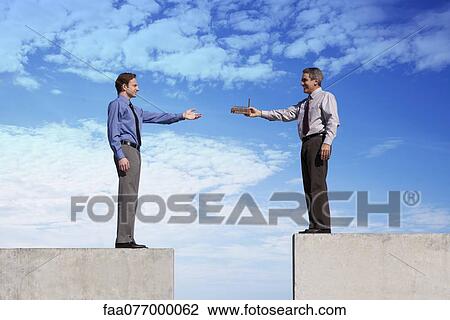 Stock Image - Businessmen standing on platforms, one handing the other a tiny factory. Fotosearch